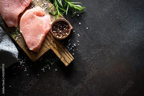 Turkey steaks with spices and herbs at wooden board at black stone table. Top view with copy space.