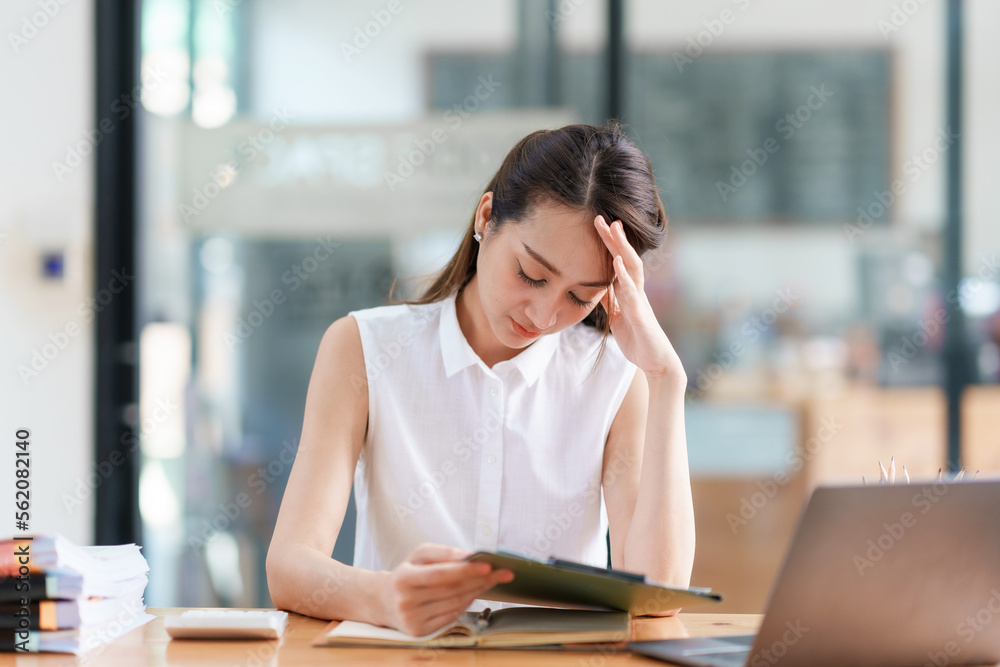 Young Asian businesswoman sitting stressed at work solving problems in different parts of the job. Young Asian businesswoman sitting stressed at work solving problems in different parts of the job.
