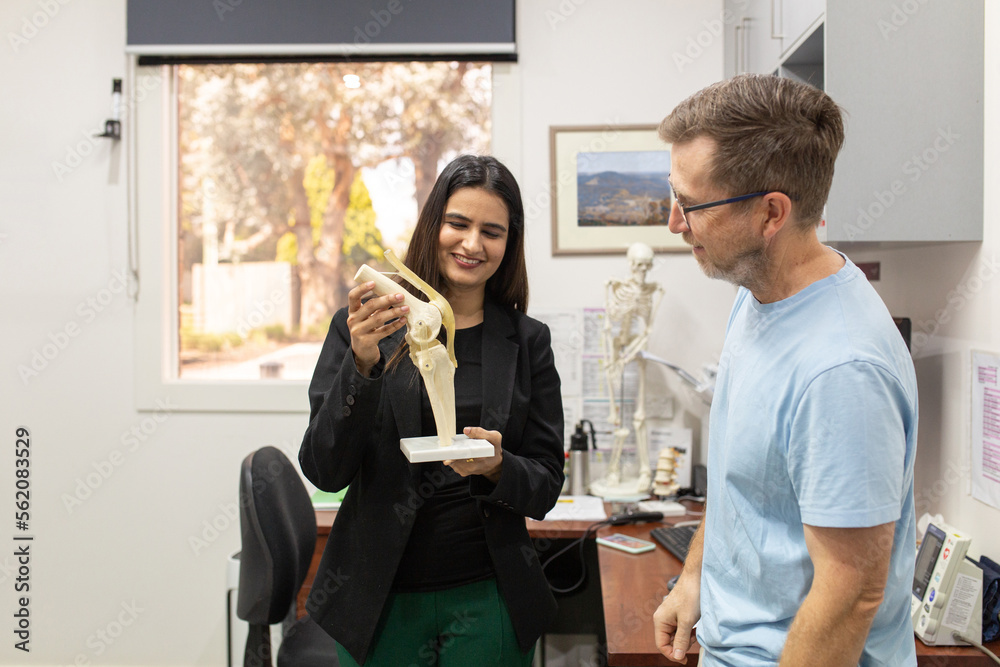 smiling woman holding a knee joint model and showing it to a man in the clinic smiling woman holding a knee joint model and showing it to a man in the clinic