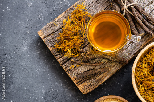 Glass cup of licorice tea with licorice root and fiber on rustic background, alternative medicine ( glycyrrhiza glabra )