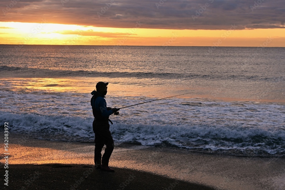 An angler aiming for flounder who is throwing and fishing on the beach at dawn.
