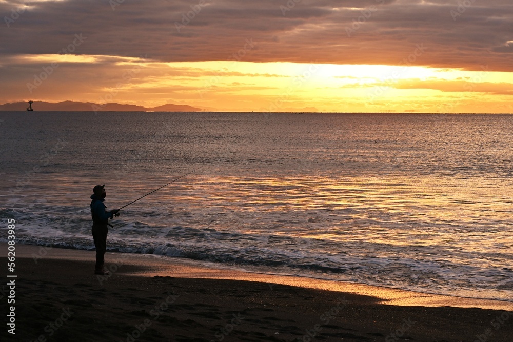 An angler aiming for flounder who is throwing and fishing on the beach at dawn.