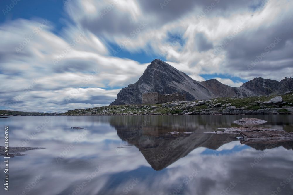 Alpine lake with mountain reflection under fast moving clouds - Long exposure - Italian alps.	
