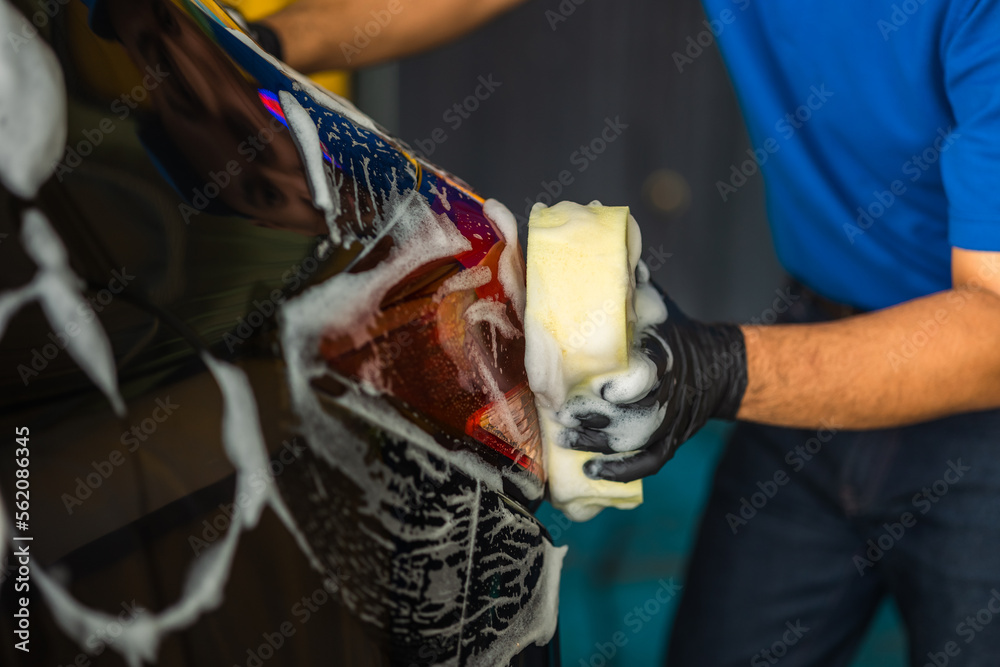 Fototapeta premium Man worker washing car service with foam and sponge. Car wash cleaning wipe station. Employees clean a vehicle professionally.