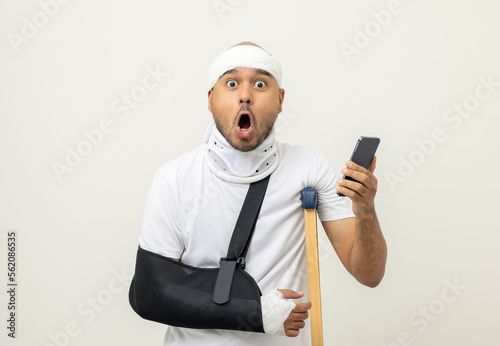 Happy young asian man broken arm holding smartphone. Asian man put on plaster bandage cast splint. Male patient wearing sling support arm after accident injury. life insurance and accident photo