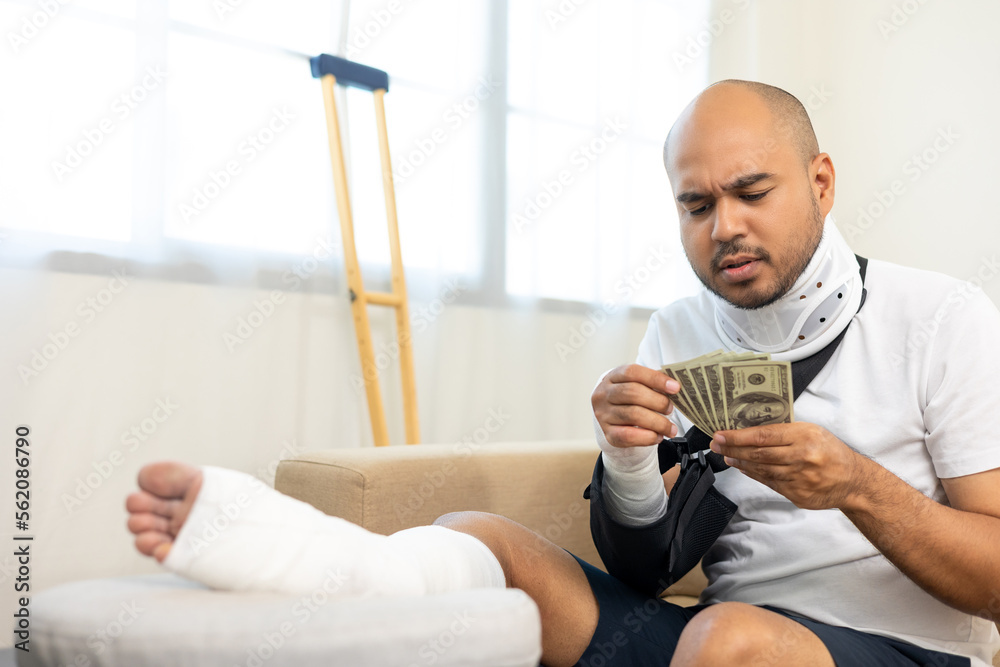 Man stressed over medical expenses money from accident fracture broken bone injury with leg splints in cast neck splints collar sling support arm. Social security and health insurance concept.