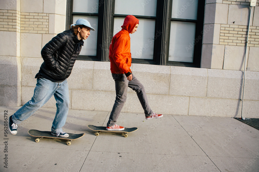 Friends skateboarding on sidewalk in city Friends skateboarding on sidewalk in city