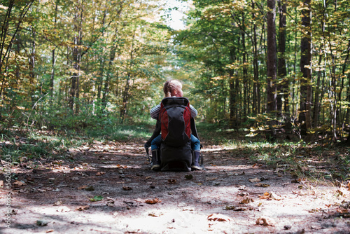 Rear view of girl with backpack sitting on bag at dirt road amidst forest photo
