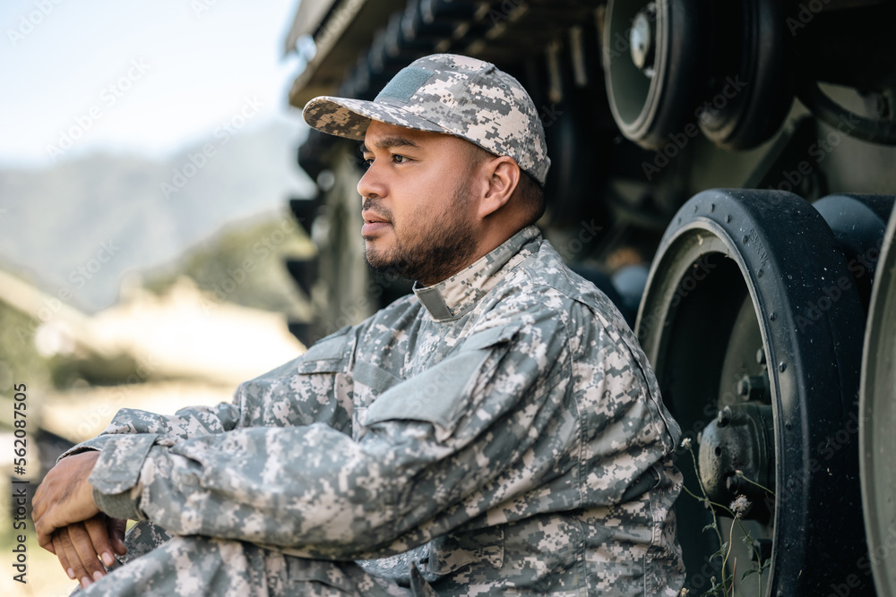 Asian man special forces soldier against on the field Mission. Commander Army soldier military defender of the nation in uniform sitting near battle tank while state of war.