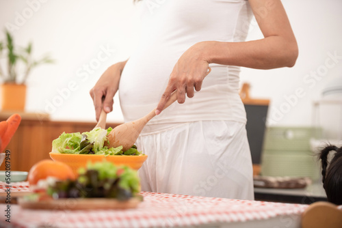 young pregnant woman makes herself salad of fresh vegetables, the concept of proper nutrition. high quality photo. pregnant woman in kitchen making salad.