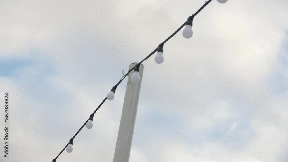 Garland with led lamps on high pole under cloudy sky in city park low angle shot. Outdoor decoration on street Garland with led lamps on high pole under cloudy sky in city park low angle shot. Outdoor decoration on street