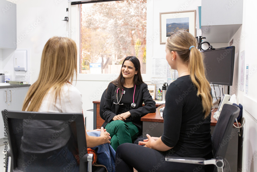 smiling female doctor in a clinic with stethoscope around her neck talking to two women smiling female doctor in a clinic with stethoscope around her neck talking to two women