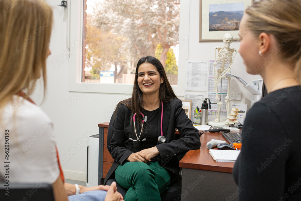 © Austockphoto - smiling female doctor in a clinic with stethoscope around her neck talking to two women