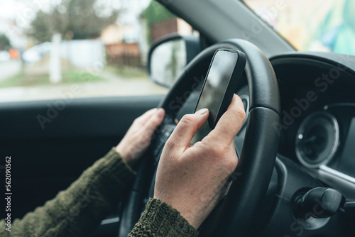Closeup shot of female hand typing message on smartphone device, casual woman driver wearing green knitted sweater using mobile phone in vehicle interior