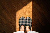 Top view of male feet wearing home slippers and standing on hardwood flooring in living room