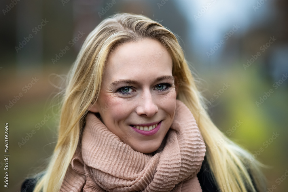 Woman young blond head portrait, warmly dressed with a scarf smiles at the camera..