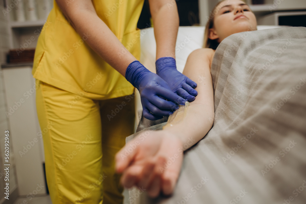 Depilation and depilation of women's hands with liquid sugar paste with a spatula. The beautician's hand applies wax paste to the armpit. The concept of smooth armpits Depilation and depilation of women's hands with liquid sugar paste with a spatula. The beautician's hand applies wax paste to the armpit. The concept of smooth armpits