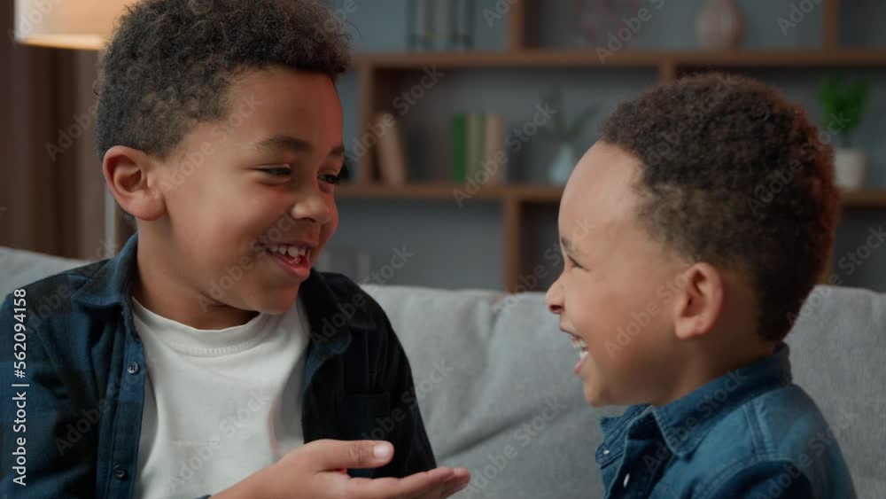 Two little boys friendly talking laughing at home. Ethnic African American multiracial multiethnic male kids schoolboys pupils sons indoors talk laugh together. Children brothers friends conversation