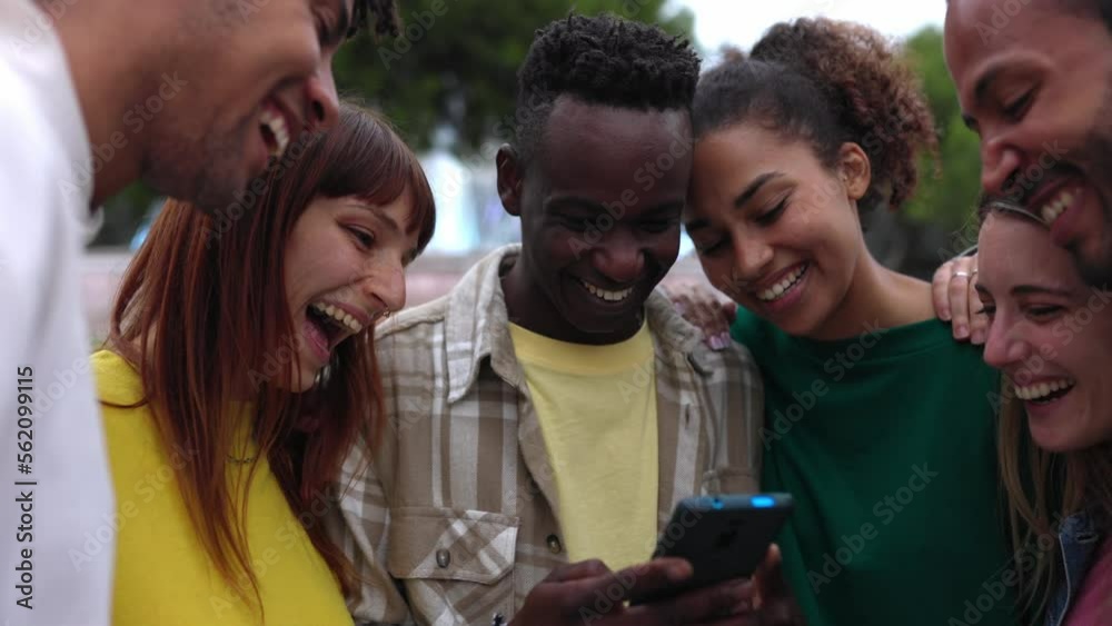 Young happy student friends having fun together using mobile phone standing outdoors. Multi-ethnic group of millennial people laughing while watching funny social media content on smartphone app. Young happy student friends having fun together using mobile phone standing outdoors. Multi-ethnic group of millennial people laughing while watching funny social media content on smartphone app.