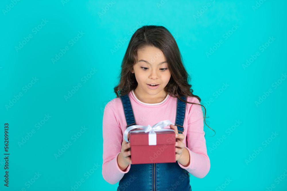 amazed girl with birthday gift isolated on blue. girl with birthday gift in studio. amazed girl with birthday gift isolated on blue. girl with birthday gift in studio.