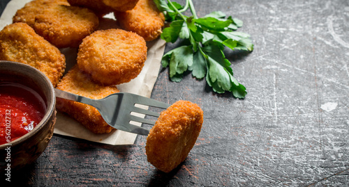 Chicken nuggets on paper and fork with sauce and parsley.