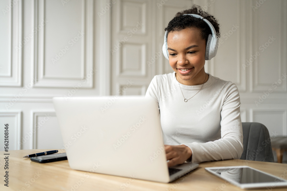 An attractive, sweet, smiling young woman holds an online meeting in the office with headphones and uses a laptop. An attractive, sweet, smiling young woman holds an online meeting in the office with headphones and uses a laptop.