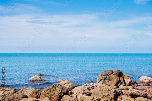 Rock in the smooth sea or ocean with clear cloud and blue bright sky background at the sandy beach on summer time