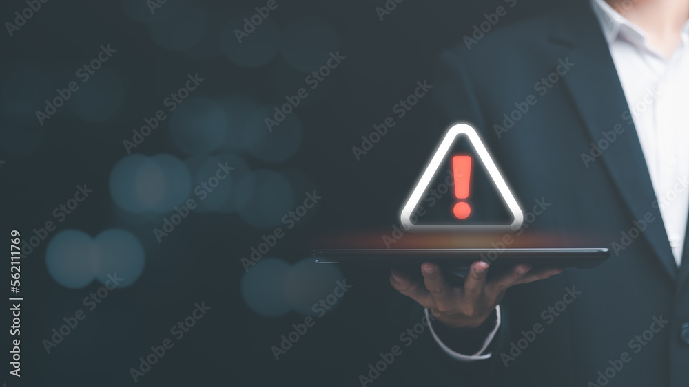 Businessman holding a tablet and showing a warning icon, exclamation mark,alarm,computer virus detected,danger warning concept or information error that should be urgently fixed and repaired - obrazy, fototapety, plakaty 