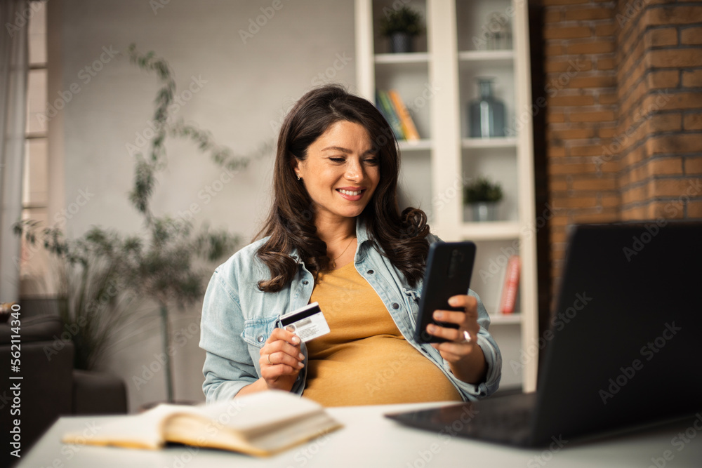 © JustLife - Pregnant woman shopping online at home. Happy woman with laptop and credit card.