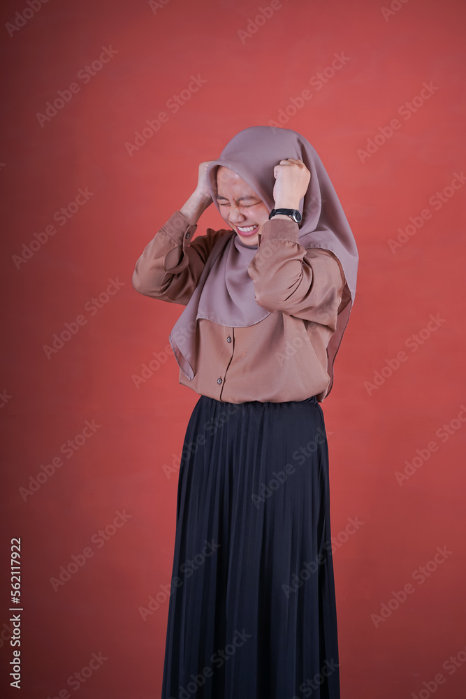 Beautiful Asian woman in brown shirt and hijab showing depressed expression on brown background