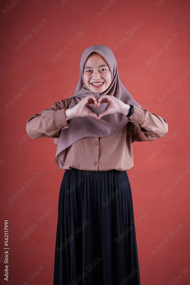 Beautiful Asian woman in brown shirt and hijab feeling happy and romantic shape heart gesture expressing tender feelings on brown background Beautiful Asian woman in brown shirt and hijab feeling happy and romantic shape heart gesture expressing tender feelings on brown background
