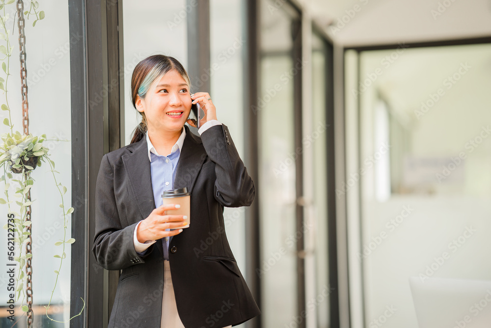 Attractive asian businesswoman or accountant holding cup of coffee and talking on the phone with her business clients while working in the office vertical image Attractive asian businesswoman or accountant holding cup of coffee and talking on the phone with her business clients while working in the office vertical image