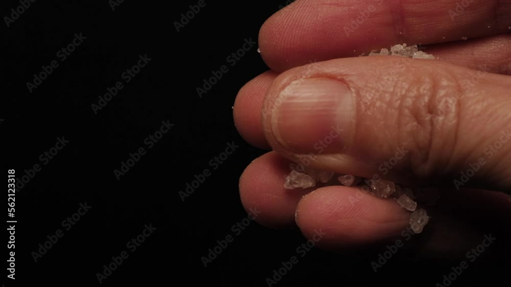 pouring grains of sea salt. close up of fingers. hand that cooking. falling salt grains in  black background. vertical view
