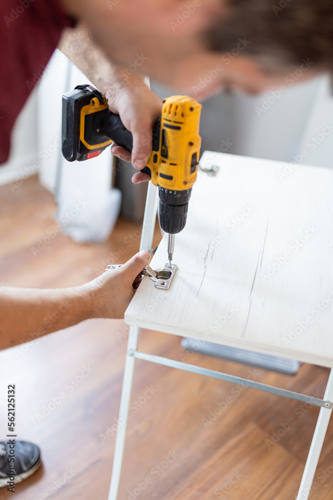 Close up of man assembling furniture by using cordless screwdriver