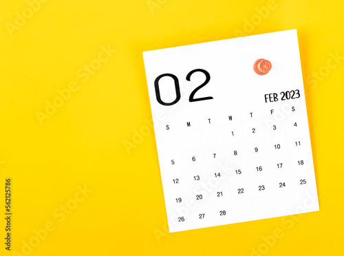 The February 2023 calendar and wooden push pin on yellow background.