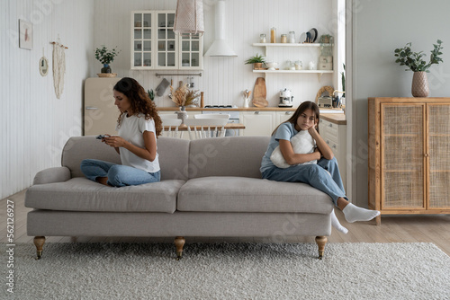 Focused busy woman mother using smartphone during family time child daughter at home. Working from home mom looking and mobile phone screen, ignoring sad upset teen girl kid. Parents and screen time photo