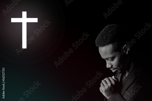 Fotobehang African man in suit is praying and giving thanks to god in dark room with crucif