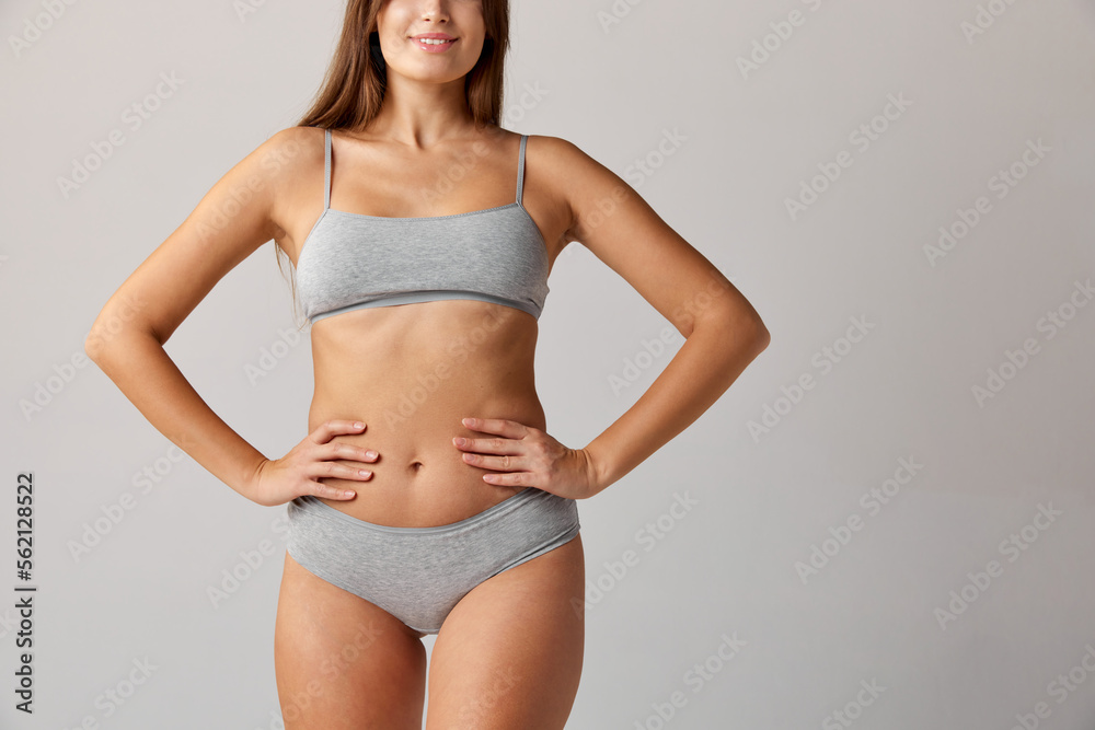 Obraz premium Cropped image of slim female body, breast, belly and buttocks in cotton underwear over grey studio background. Concept of body and skin care, fitness