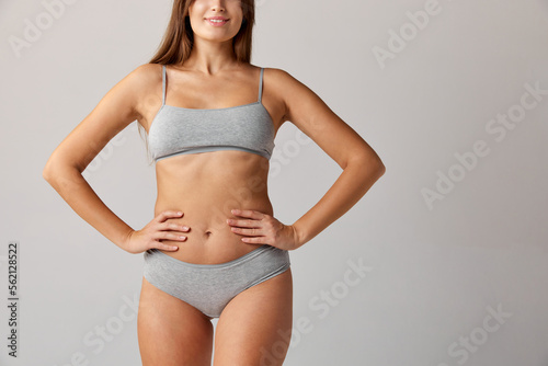Cropped image of slim female body, breast, belly and buttocks in cotton underwear over grey studio background. Concept of body and skin care, fitness