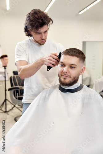 Barber trim hair with clipper on handsome bearded man