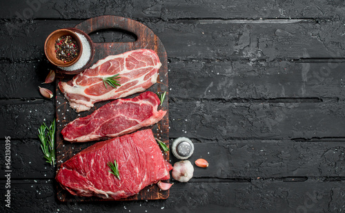 Raw meat. Beef and pork steaks with spices on the cutting Board.
