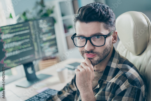 Photo of cheerful positive coder dressed eyewear hand arm chin writing java script modern gadget indoors workplace workstation loft