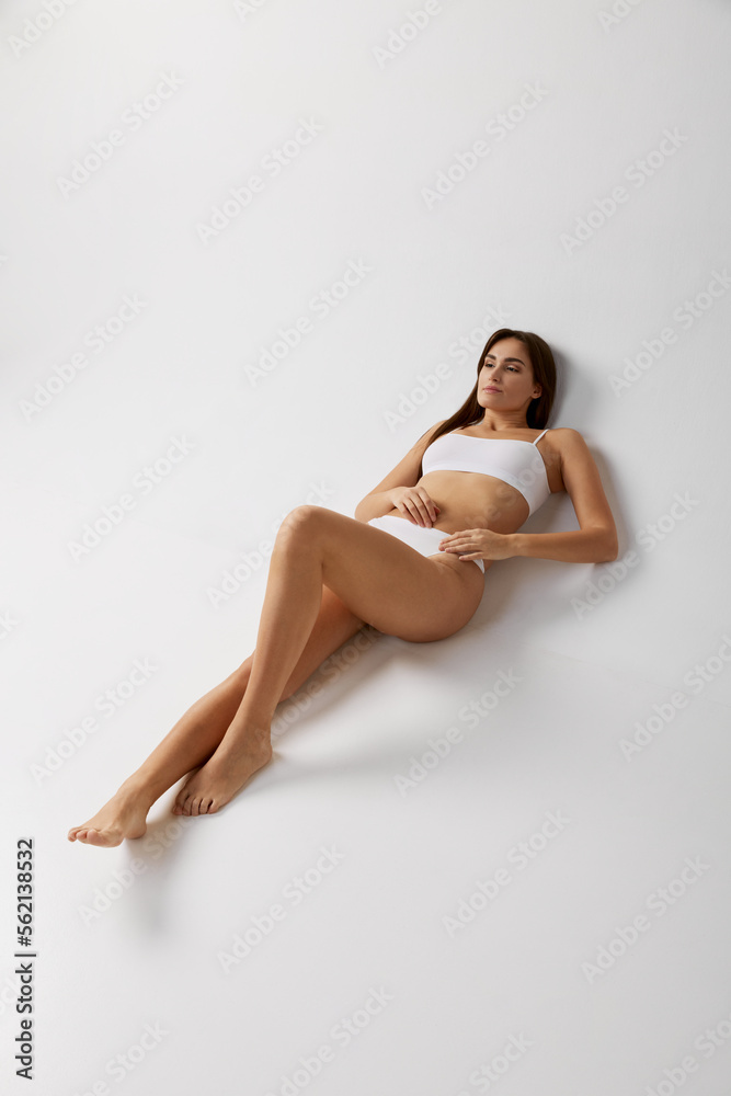 Portrait of young beautiful girl posing in white underwear over grey studio background. Slender body. Concept of body and skin care, fitness