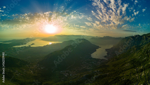 Panorama of dazzling sun in the evening sky illuminates all the peaks of the Balkan Montenegrin mountains and the coast of Kotor Bay