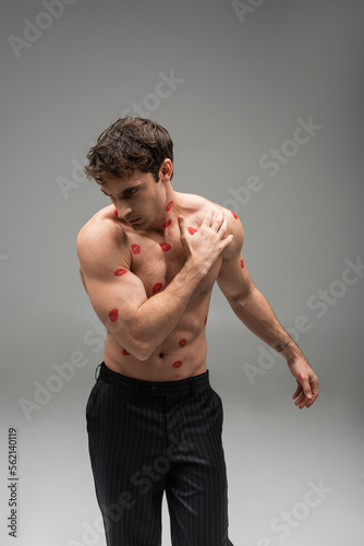 athletic man in black trousers posing with red lip prints on muscular torso on grey background. photo