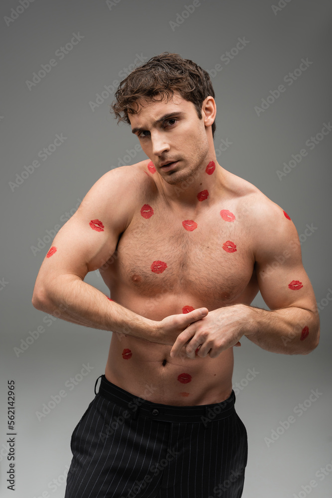 Naklejka premium athletic man with red lip prints on shirtless muscular body looking at camera on grey background.