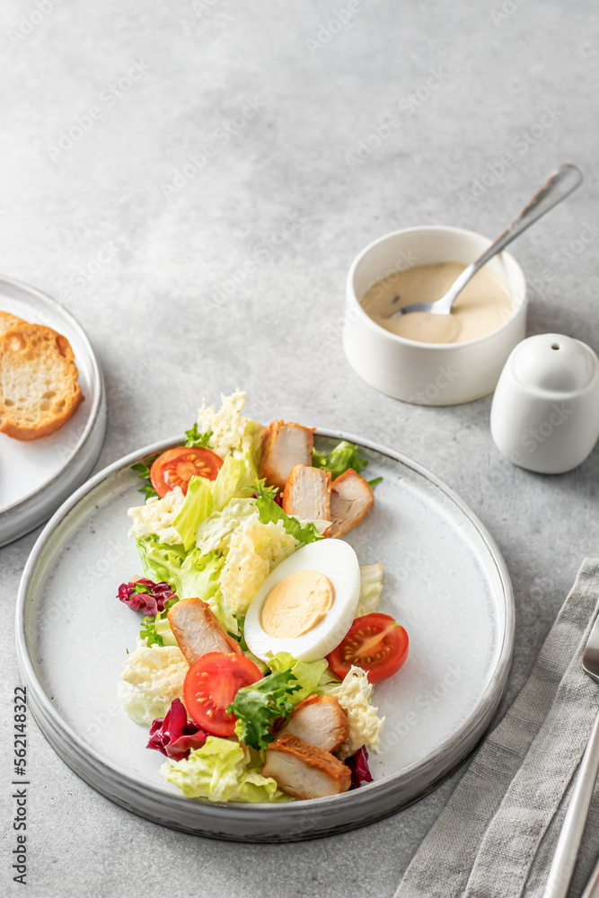 Caesar salad in modern linear feed. Healthy salad made with chicken, egg, cherry tomatoes, iceberg lettuce and parmesan chips with cutlery on gray table. Light diet dinner, text space, menu Caesar salad in modern linear feed. Healthy salad made with chicken, egg, cherry tomatoes, iceberg lettuce and parmesan chips with cutlery on gray table. Light diet dinner, text space, menu