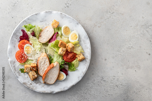 Caesar salad. Healthy salad made with chicken fillet, cherry tomatoes, iceberg lettuce, parmesan cheese and croutons on light grey background top view with copy space. Light diet dinner, text space