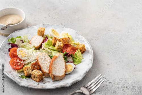 Caesar salad. Healthy salad made with chicken fillet, cherry tomatoes, iceberg lettuce, parmesan cheese and croutons on light grey background with cutlery. Light diet dinner, space for text