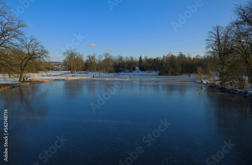 Menschen fahren Schlittschuhe auf einem gefrorenen See in einer schönen Parklandschaft bei strahlend blauem Himmel